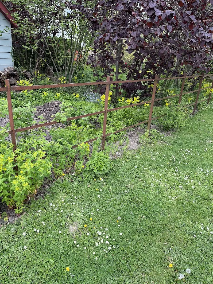 Landelijke omheining in Cortenstaal met bloeiende beplanting en gras